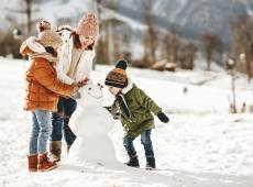 Eine Mutter baut mit den Kindern einen Schneemann im Schnee
