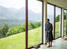 Mann steht im Bademantel an eine Säule gelehnt und genießt die Aussicht auf die Berge