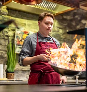 Koch schwenkt eine Pfanne mit Flammen