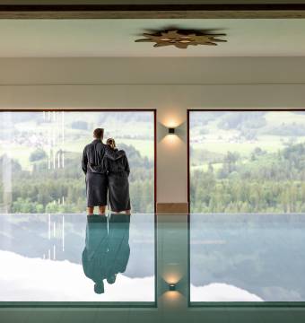 Paar im Bademantel stehen zwischen Pool und Panoramafenster