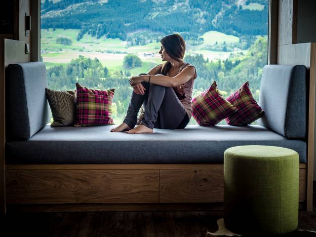 Frau sitz auf Panoramaliege im Hotelzimmer und genießt die Aussicht