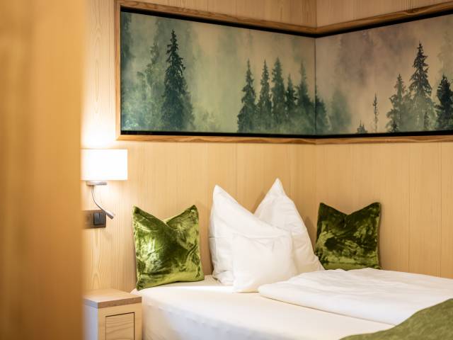 Modernes Einzelzimmer mit grünen Zierkissen und Wandbild eines Waldes