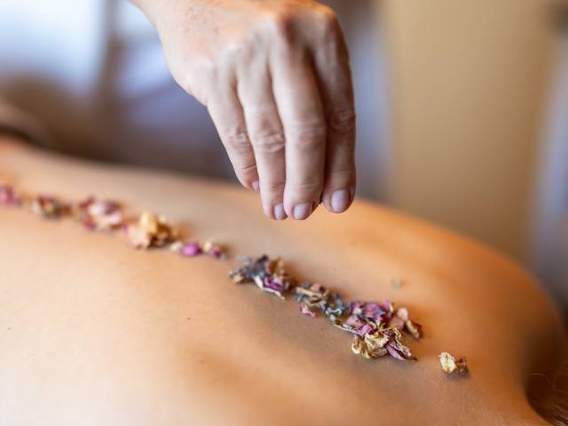 Person erhält Wellnessanwendung mit Kräutern auf ihren Rücken