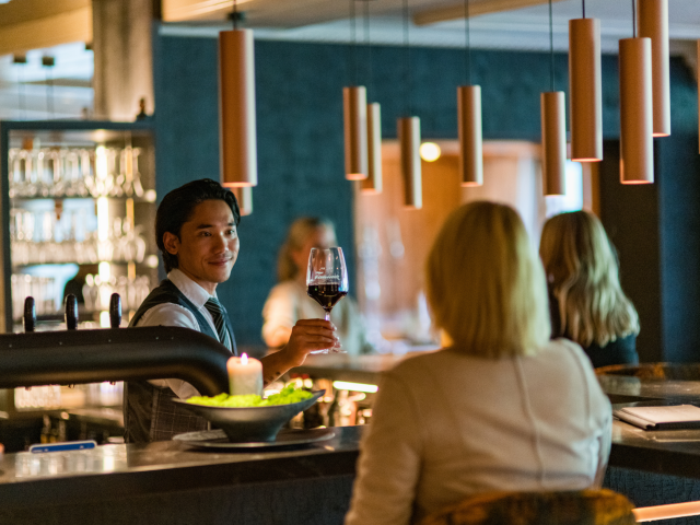 Barkeeper überreicht ein Glas Rotwein an eine Damen an der Bar