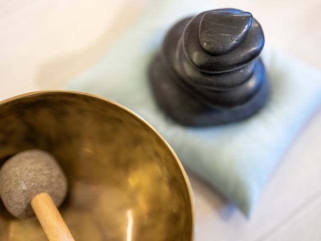 Anschnitt einer Klangschale daneben stapeln sich schwarze flache Steine